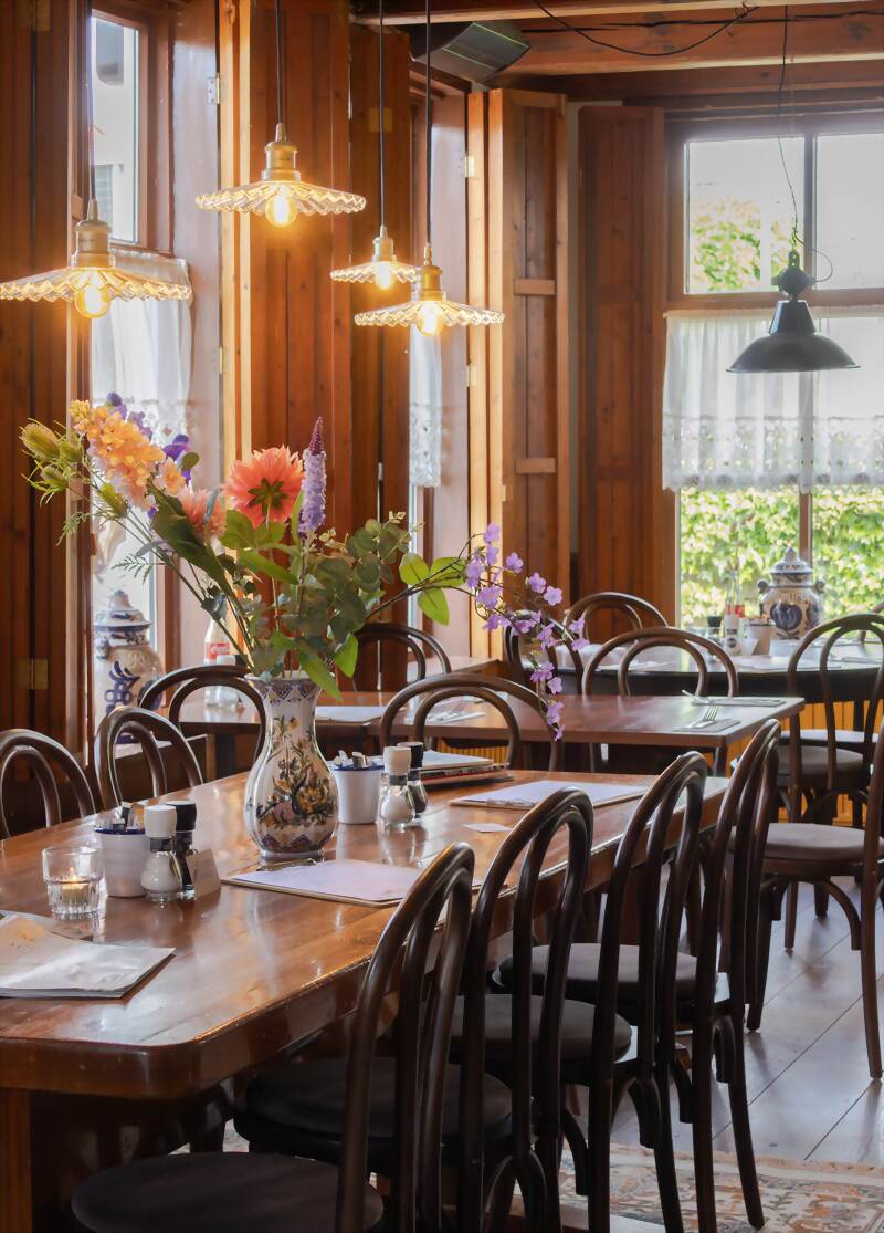 Het eetcafé met lange houten tafels, Weense stoelen en verse bloemen