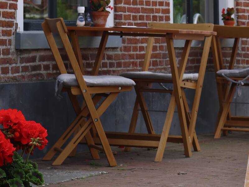 Het terras voor het café met houten klaptafels en rode geraniums
